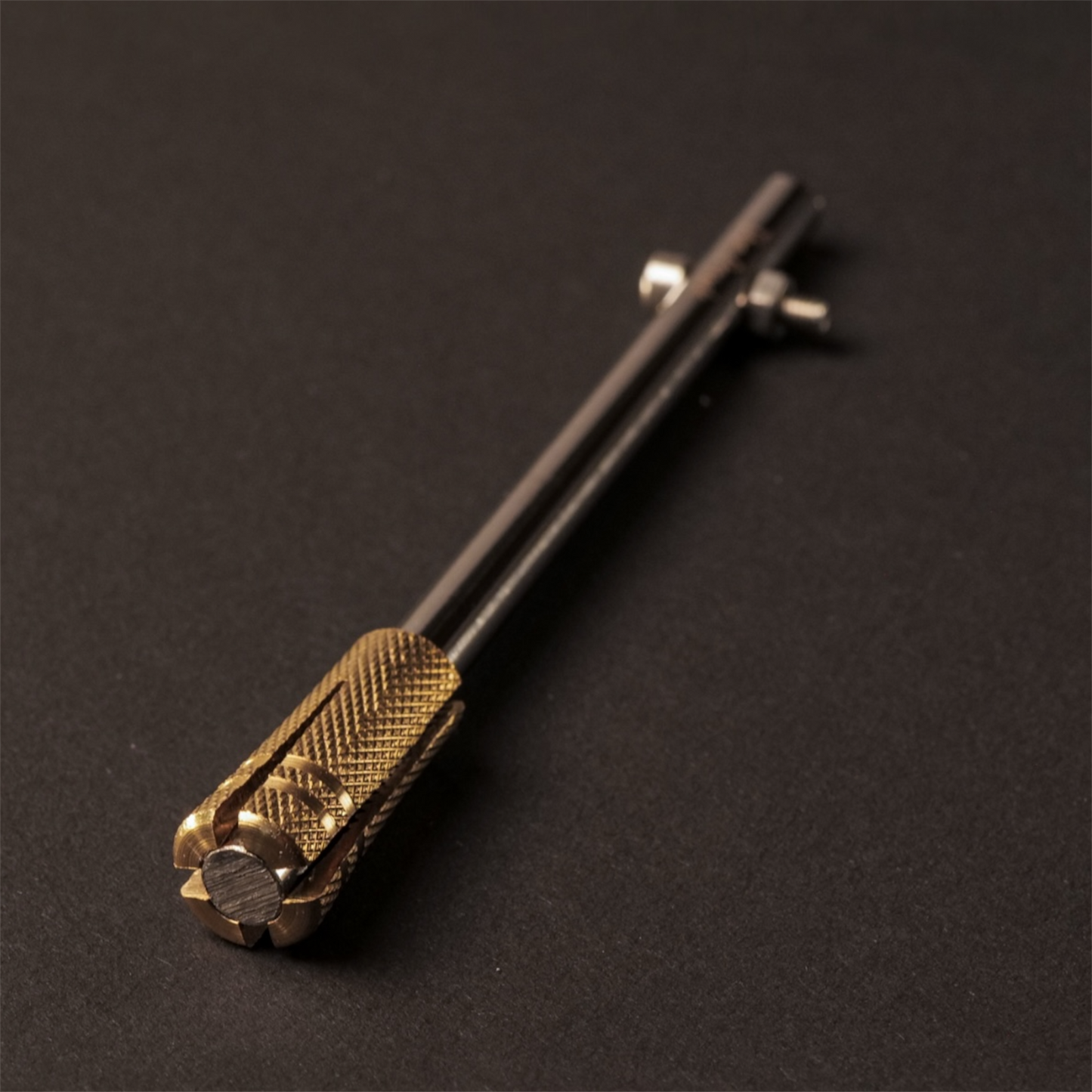The Powk handpoke tattoo tool with gold brass grip and stainless steel, aluminium needle bar on dark background