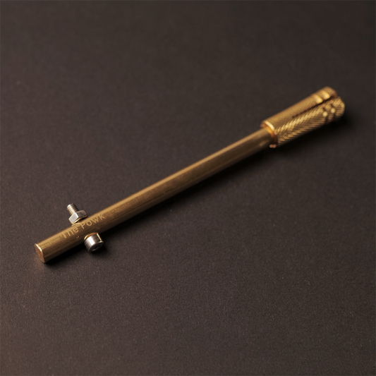 The Powk handpoke tattoo tool with gold brass grip and bronze brass needle bar on dark background