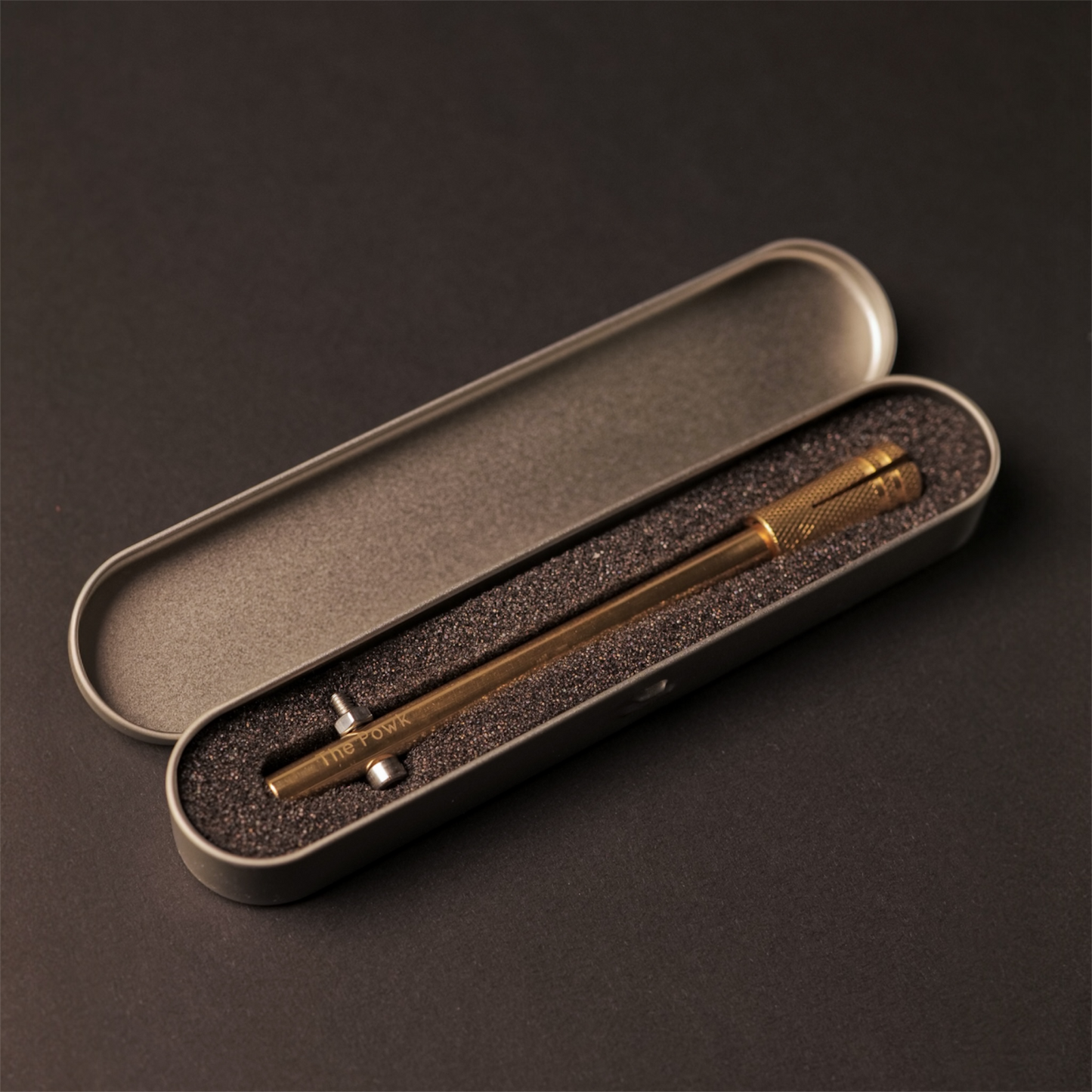 The Powk handpoke tattoo tool with gold brass grip and bronze, brass needle bar in a tin protective carry case on dark background