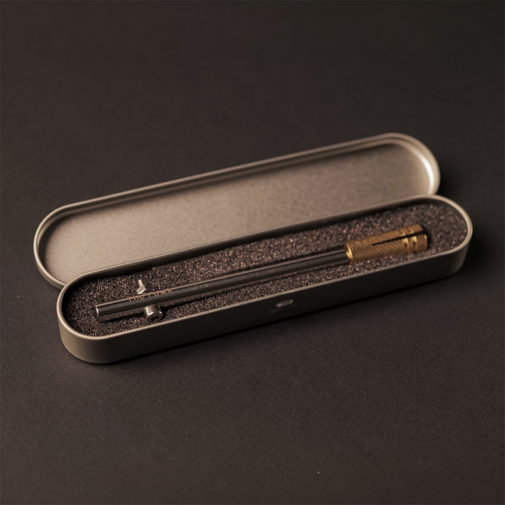 The Powk handpoke tattoo tool with gold brass grip and stainless steel, aluminium needle bar on dark background