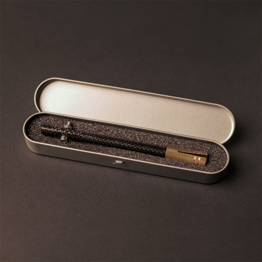 The Powk handpoke tattoo tool with gold brass grip and Carbon Fiber needle bar on dark background in a metal tin carry case 