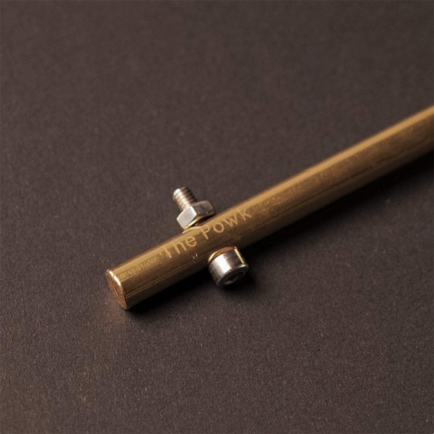 The Powk handpoke tattoo tool with gold brass grip and bronze brass needle bar on dark background