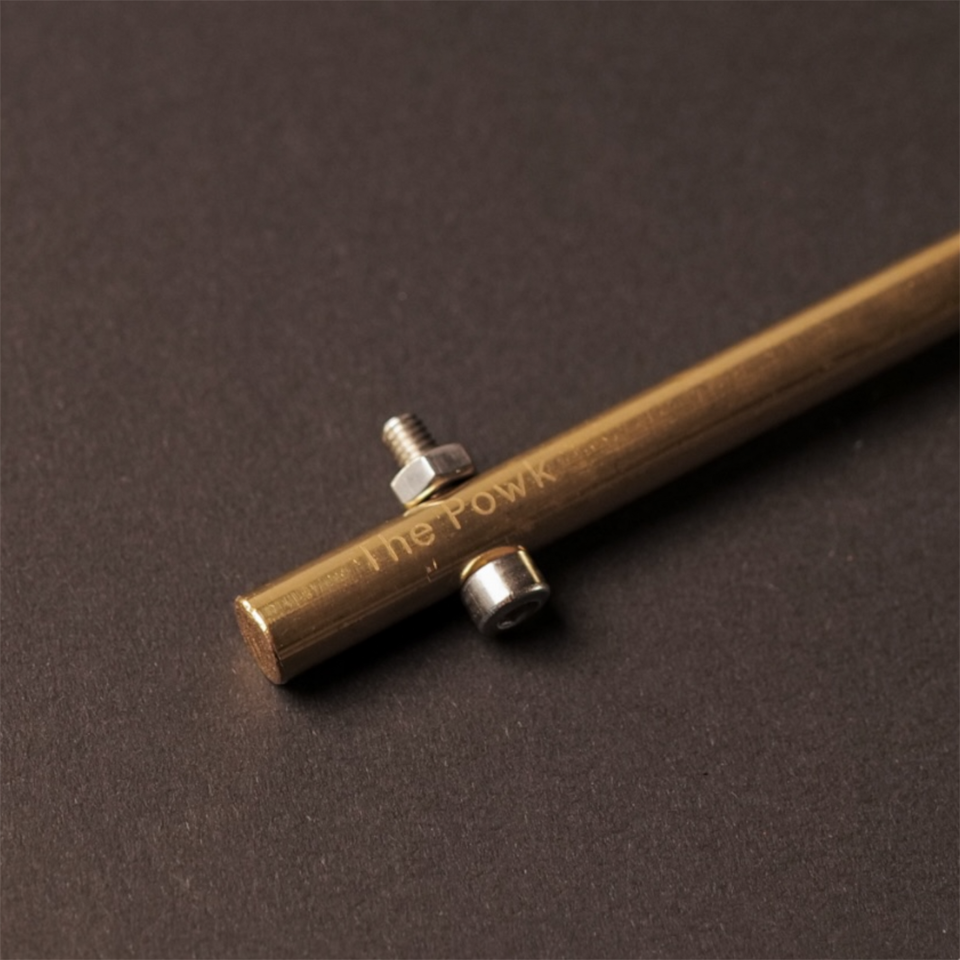 The Powk handpoke tattoo tool with gold brass grip and bronze brass needle bar on dark background