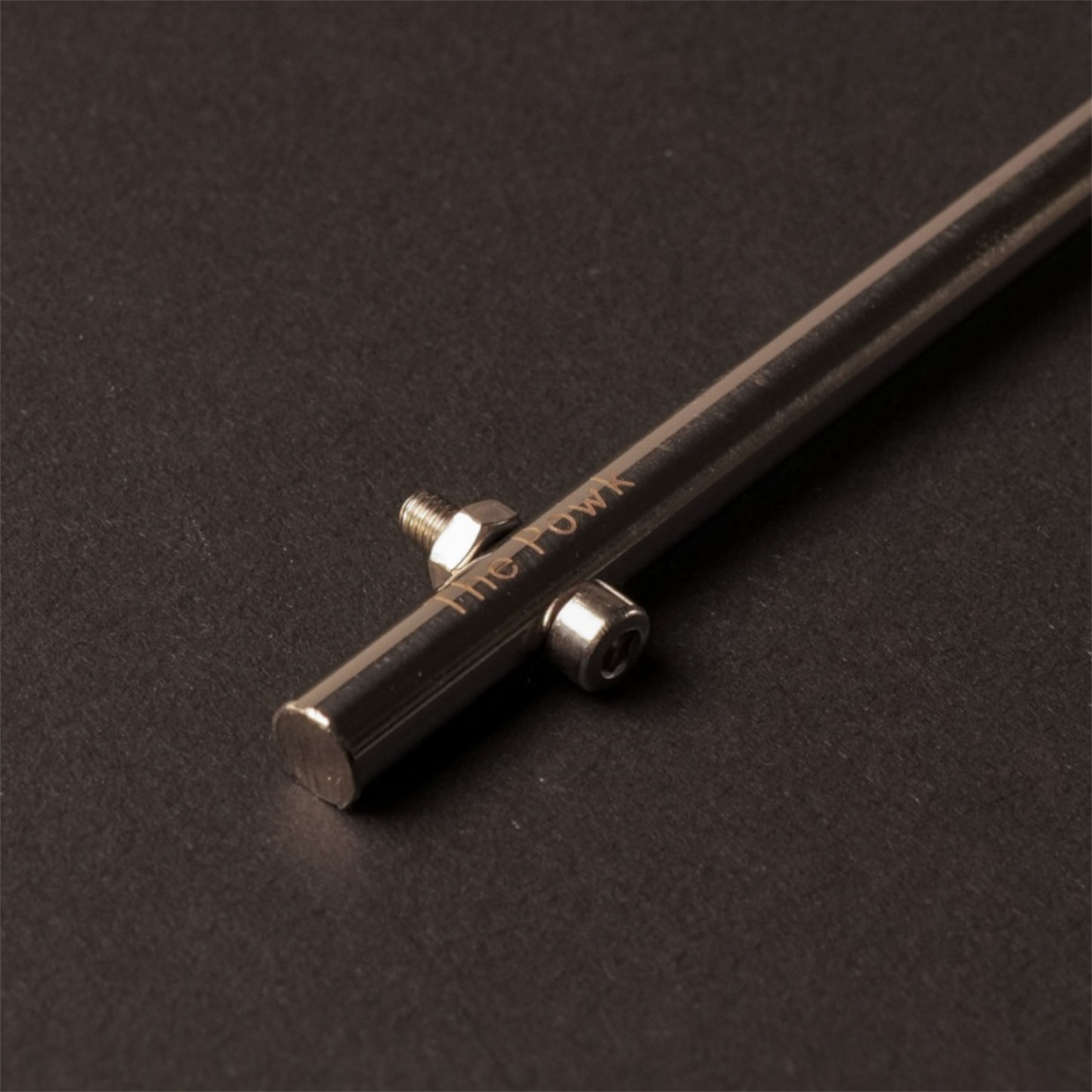 Close up of The Powk handpoke tattoo tool with gold brass grip and stainless steel, aluminium needle bar on dark background
