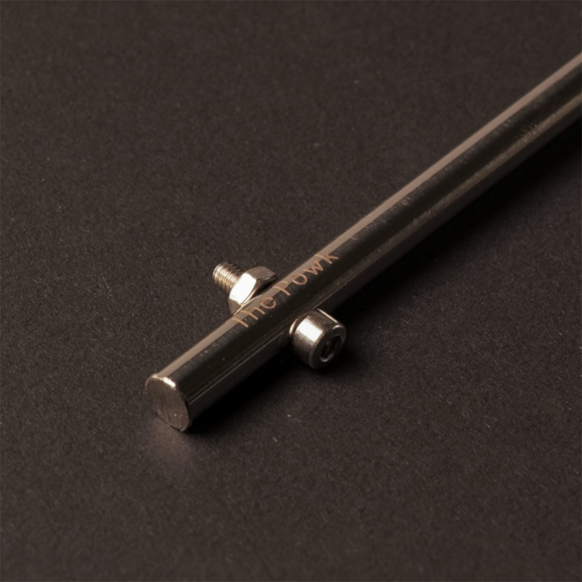 Close up of The Powk handpoke tattoo tool with gold brass grip and stainless steel, aluminium needle bar on dark background