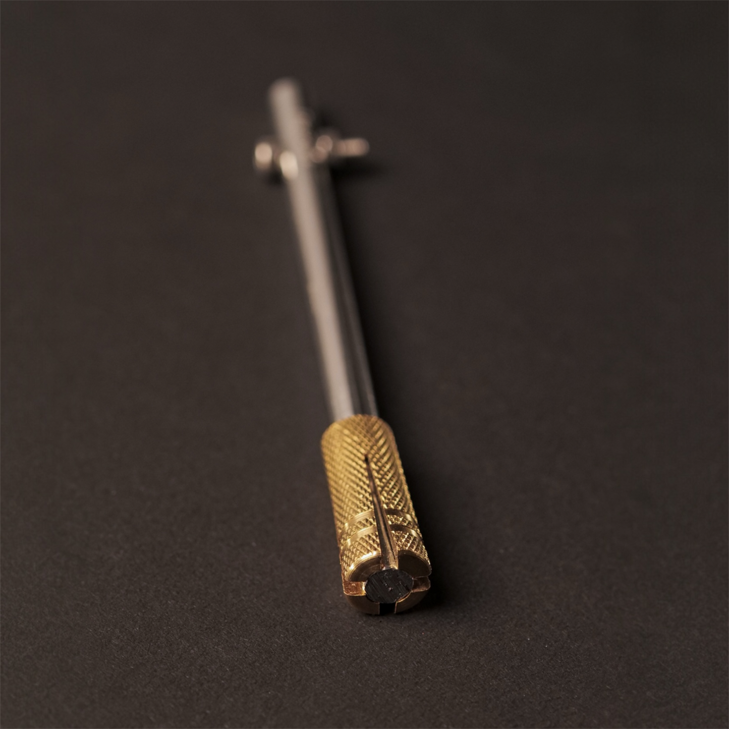The Powk handpoke tattoo tool with gold brass grip and stainless steel, aluminium needle bar on dark background