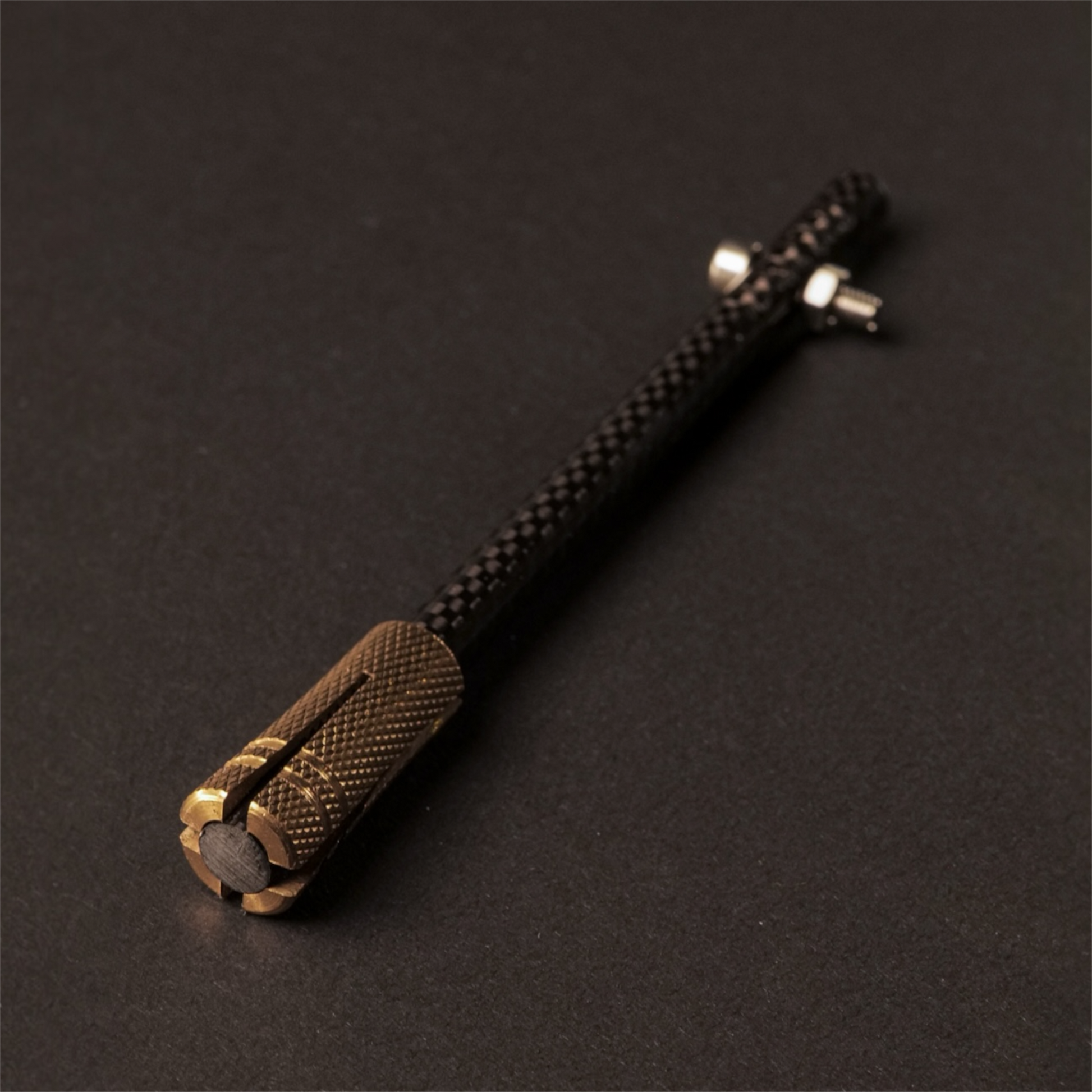 The Powk handpoke tattoo tool with gold brass grip and Carbon Fiber  needle bar on dark background