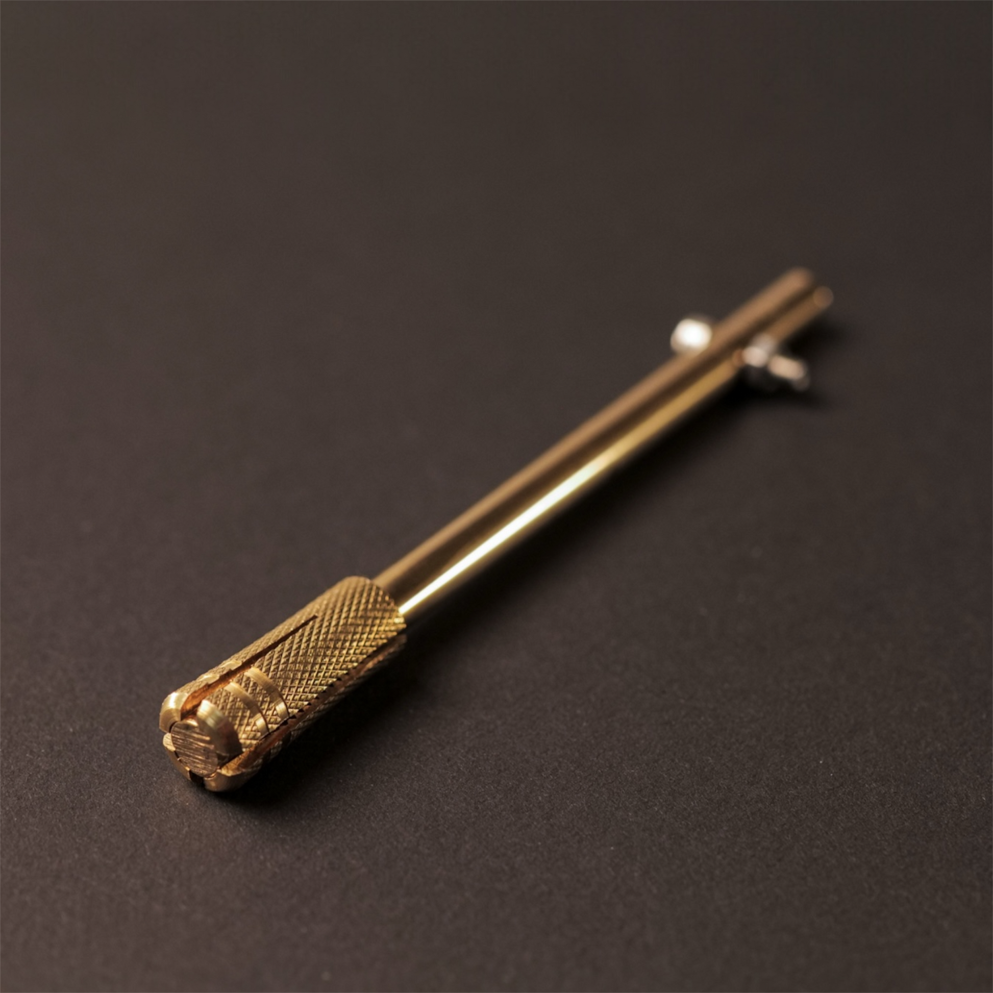 The Powk handpoke tattoo tool with gold brass grip and bronze brass needle bar on dark background